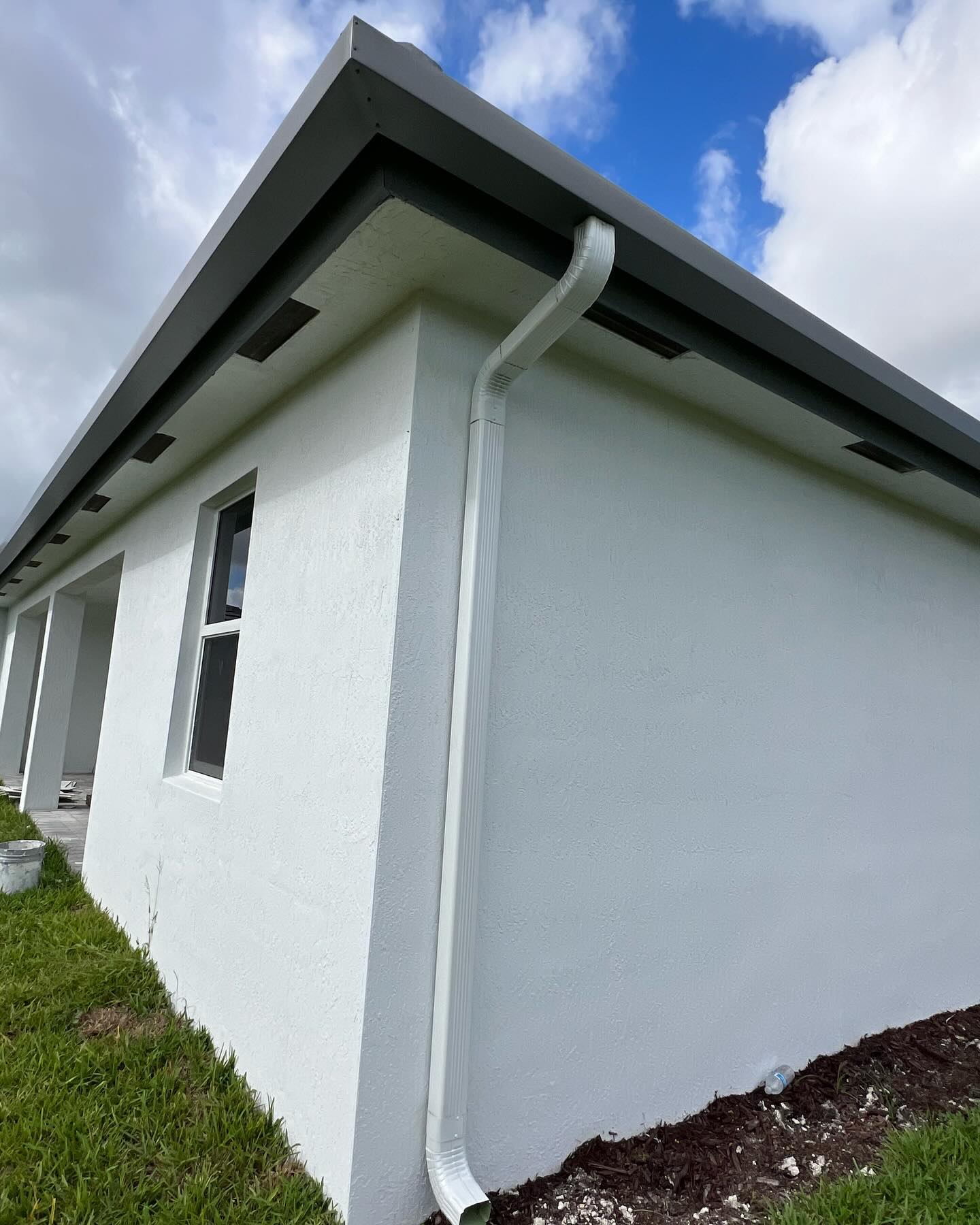 White downspout and seamless gutter on a new gray stucco home corner.