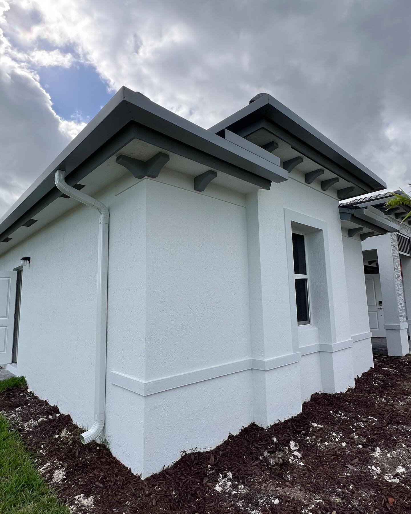 New construction home corner with white downspout and decorative gray fascia.