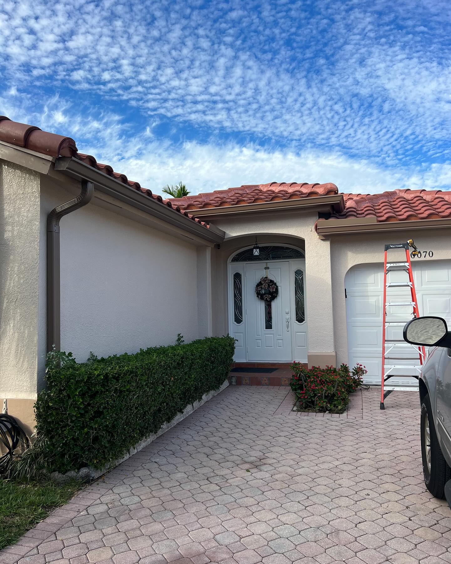 Tile-roof home entry with brown gutters and downspout; ladder staged at right.