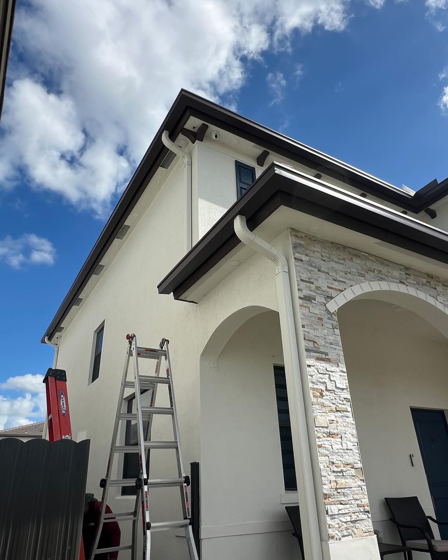 White seamless gutters and downspout along the eaves of a two-story home.