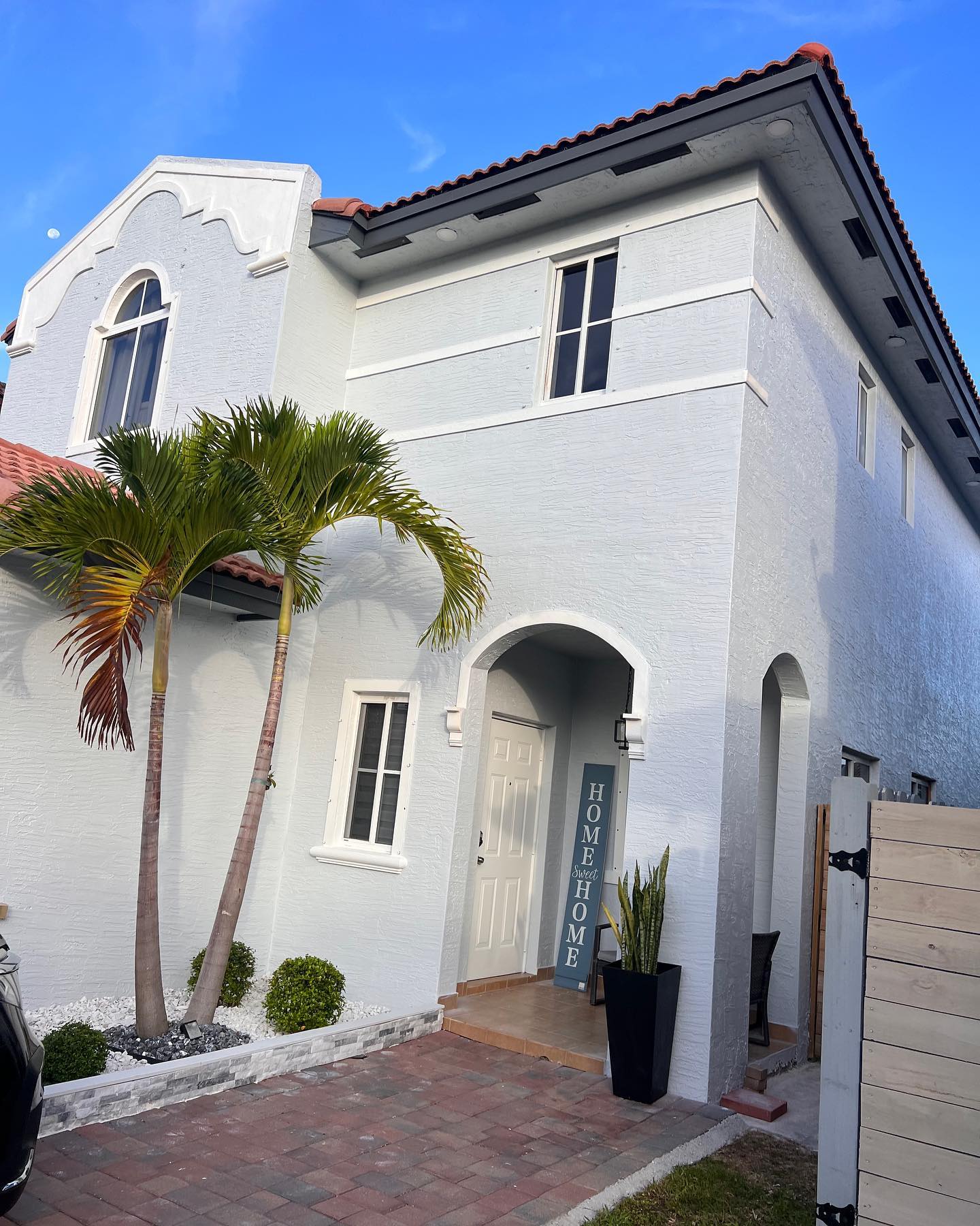 White two-story Mediterranean home with dark gutters and tile roof, blue sky