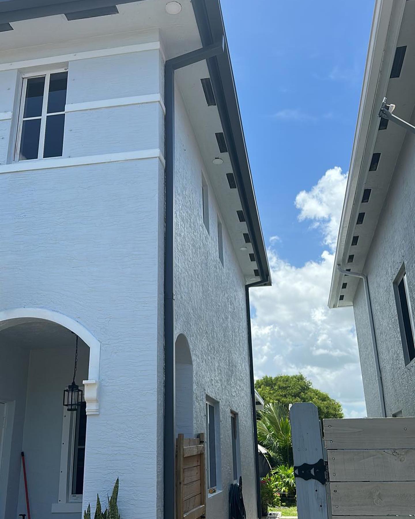 Dark gutters and downspouts along white stucco homes, bright blue sky
