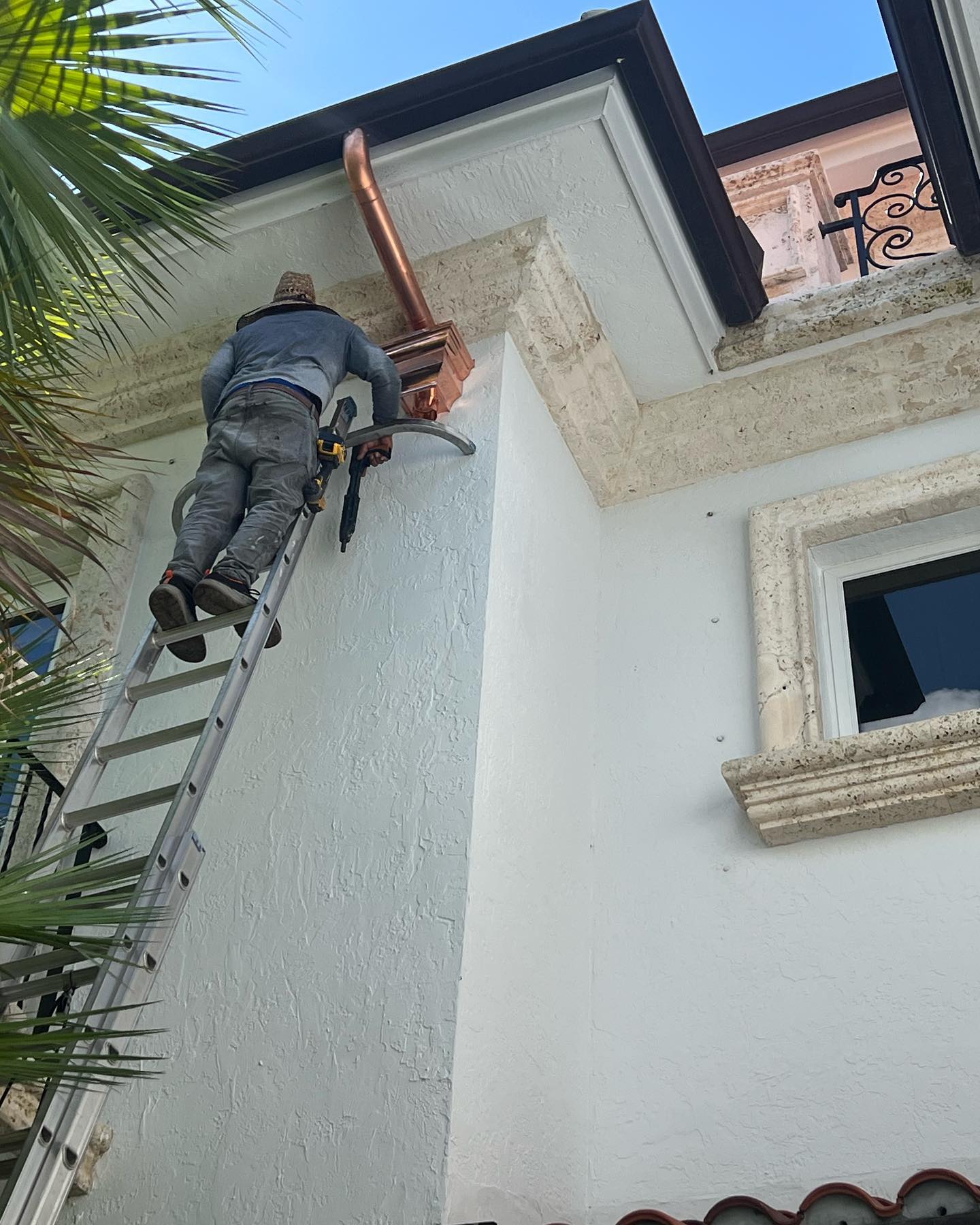 Worker on ladder installing copper downspout on upscale stucco home