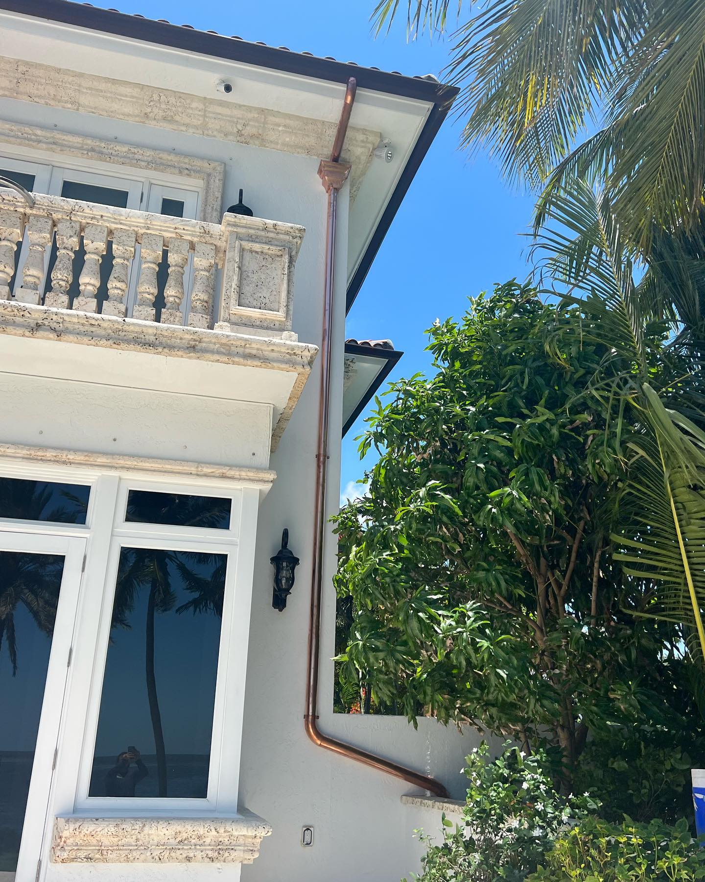 Copper downspout on white home corner with palm and tile roof, blue sky