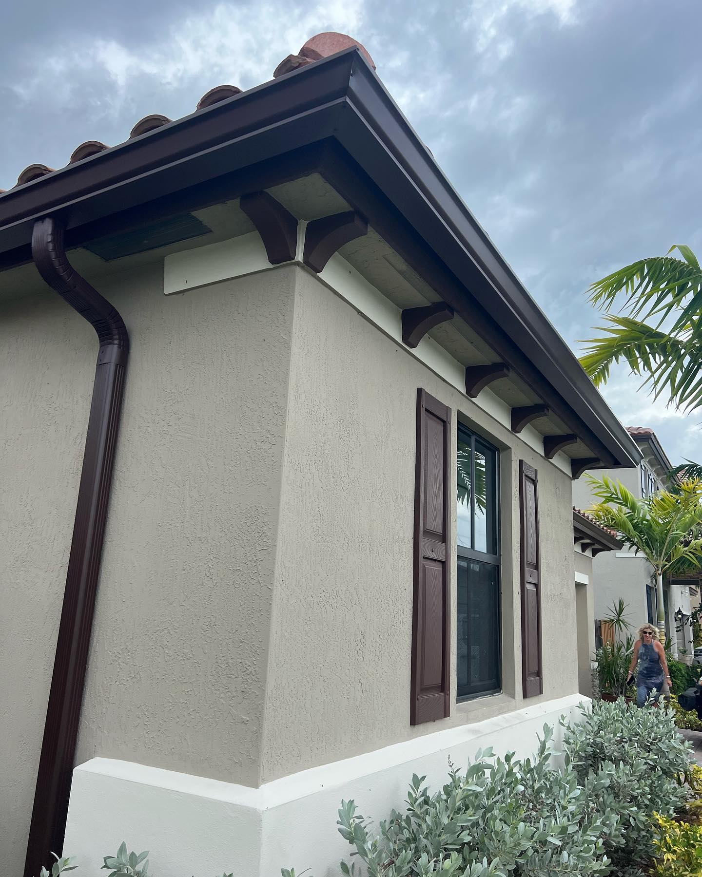 Dark brown gutter and downspout on stucco home with tile roof and brackets