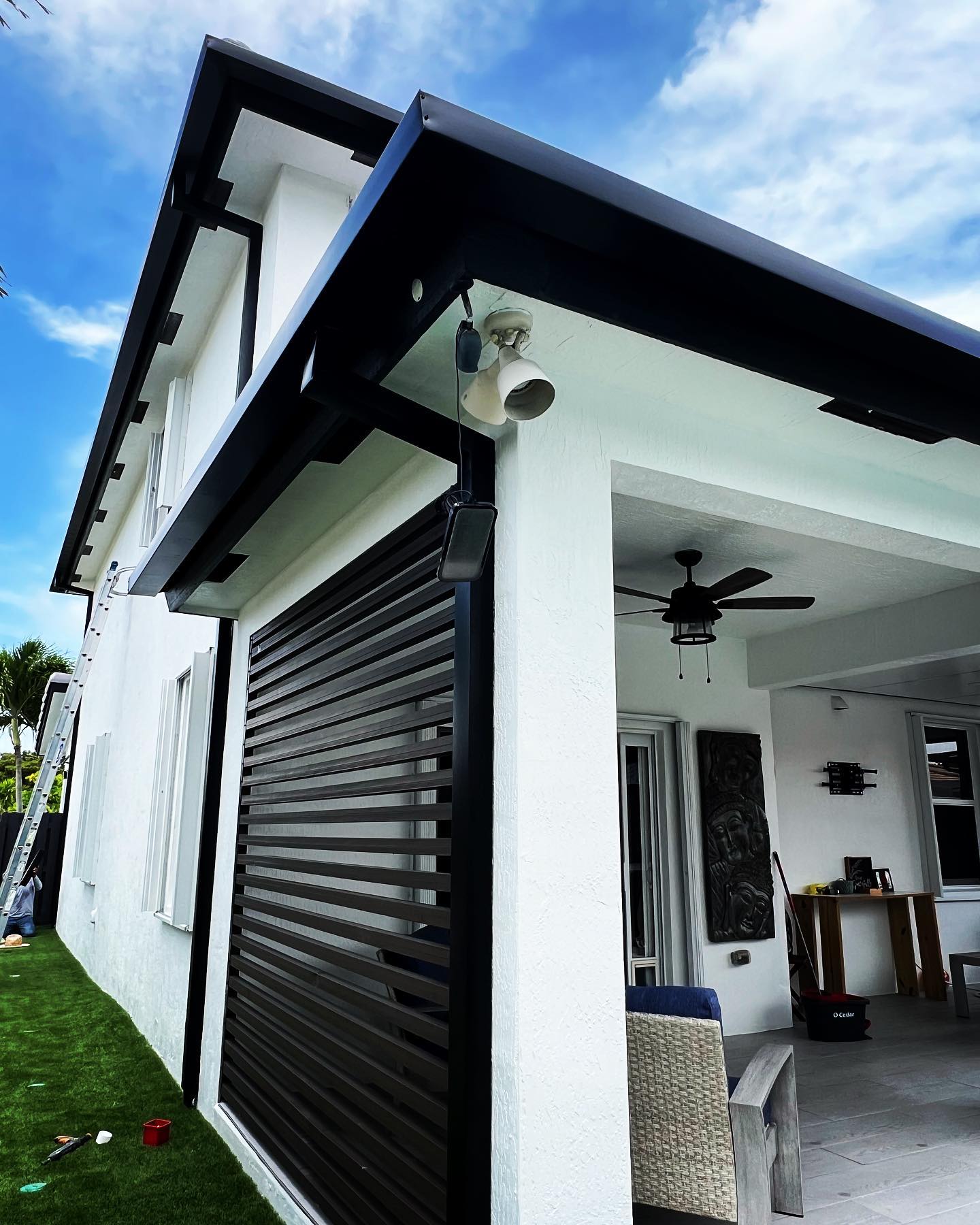 Black gutters and fascia on white home with covered patio, blue sky