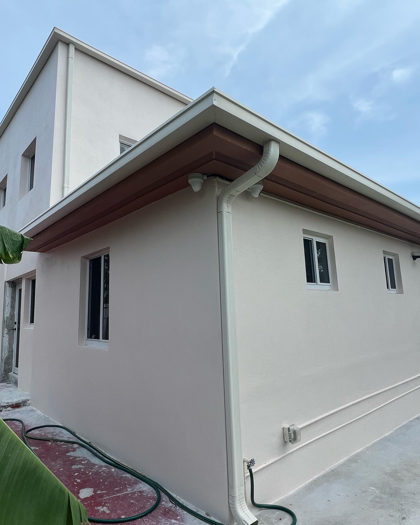 White downspout and brown fascia gutter on tan home corner, blue sky