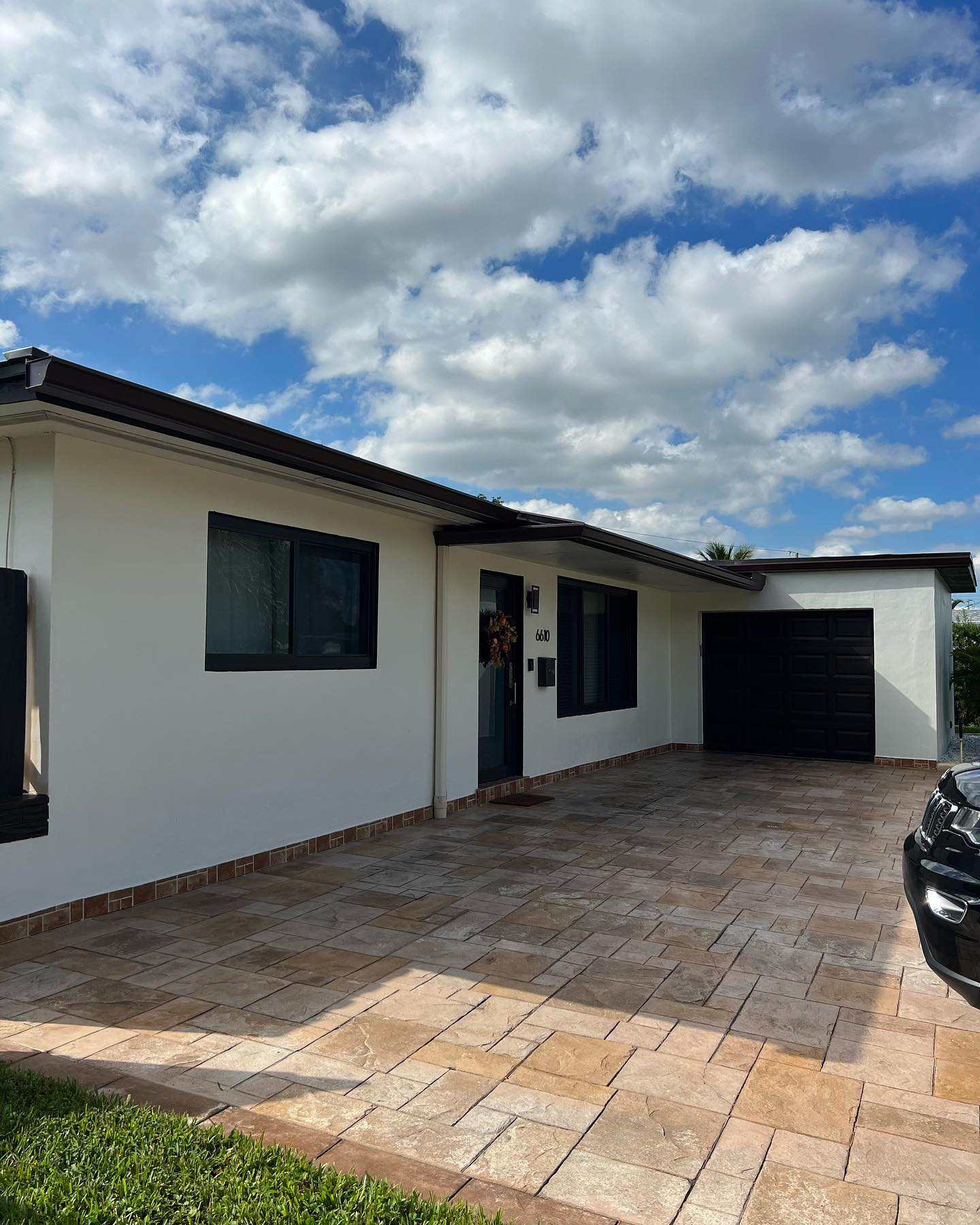 White single-story home with finished dark gutters and paver driveway under clouds.