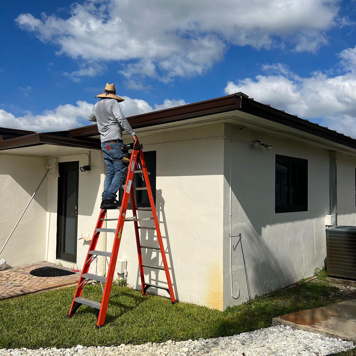 Technician on a tall ladder installing gutter at the corner of a stucco home.