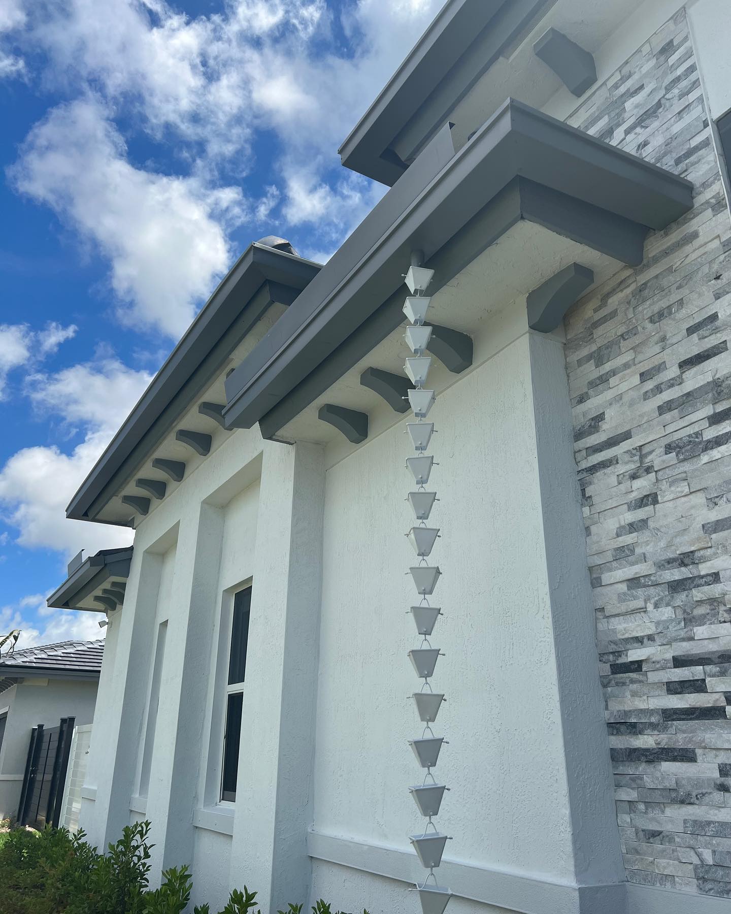 Upward view of a cup-style rain chain along a stone-and-stucco home corner.