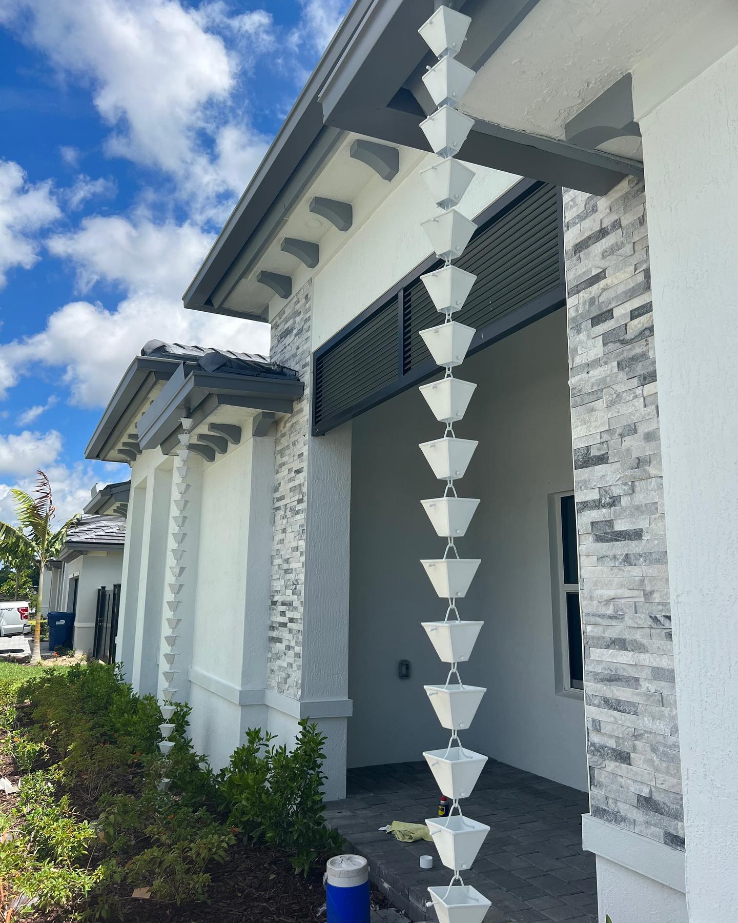 White cup-style rain chain on stone-and-stucco home exterior under blue sky.