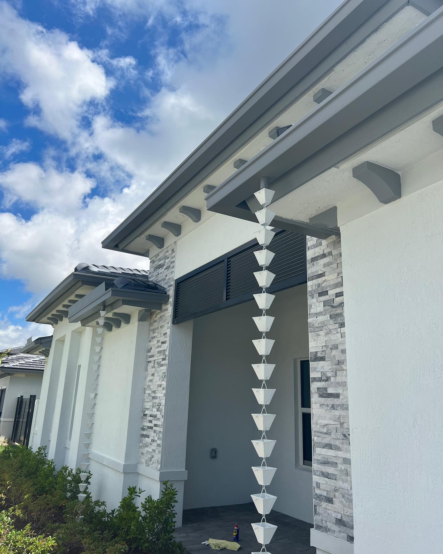 White cup rain chain descending from gray fascia on modern Florida home.