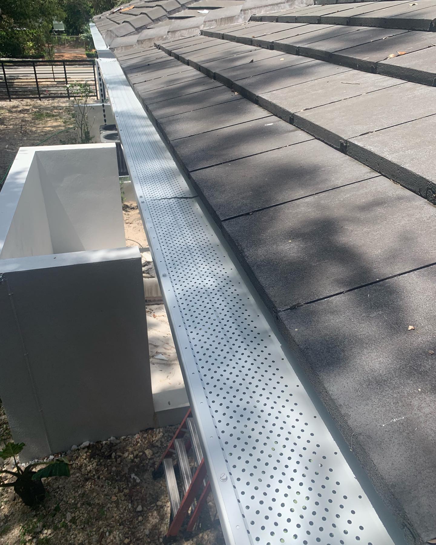 Newly installed gutter with perforated leaf-guard cover along tile roof edge.